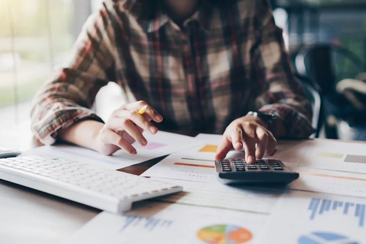 Pessoa analisando documentos financeiros e gráficos sobre uma mesa.